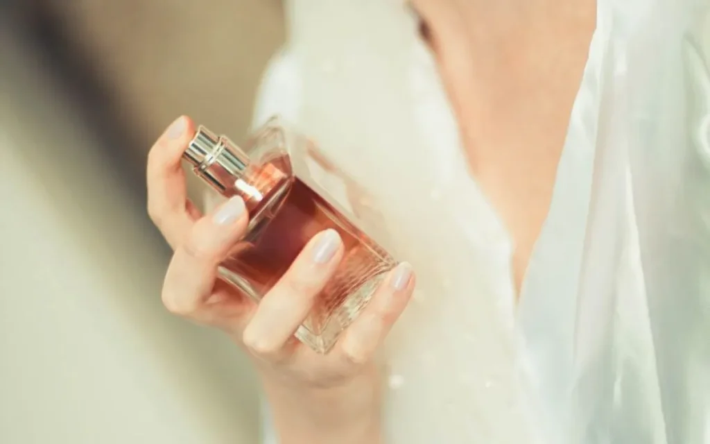 Kobieta trzymająca flakon perfum przy dekolcie